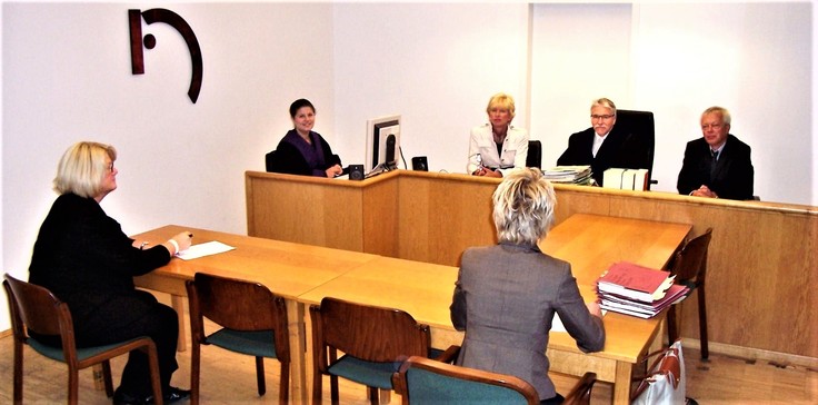 Richterbank mit Protokollführerin und Beteiligte im Sitzungssaal